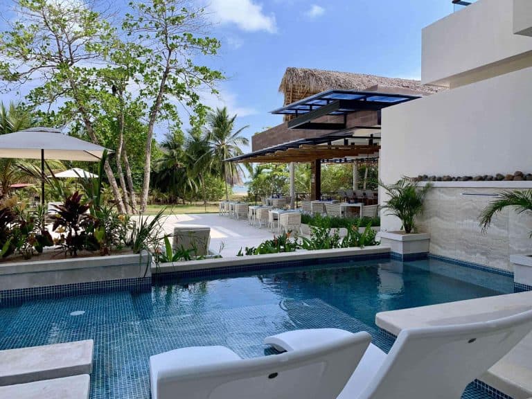 Luxury poolside lounge area with sunbeds overlooking a tropical beach setting with clear skies.