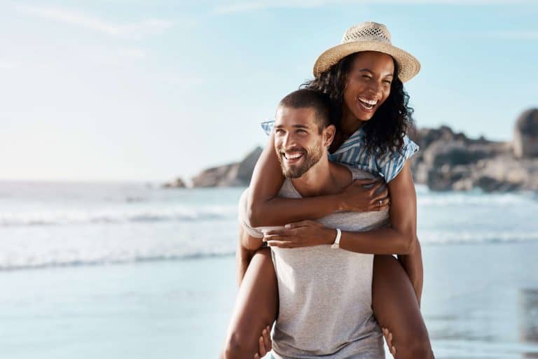 A man giving a woman a piggyback ride on a sunny beach.