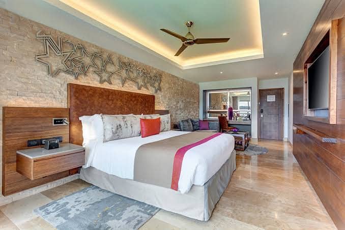 A modern bedroom with a large bed, decorative pillows, and an en-suite bathroom visible in the background.