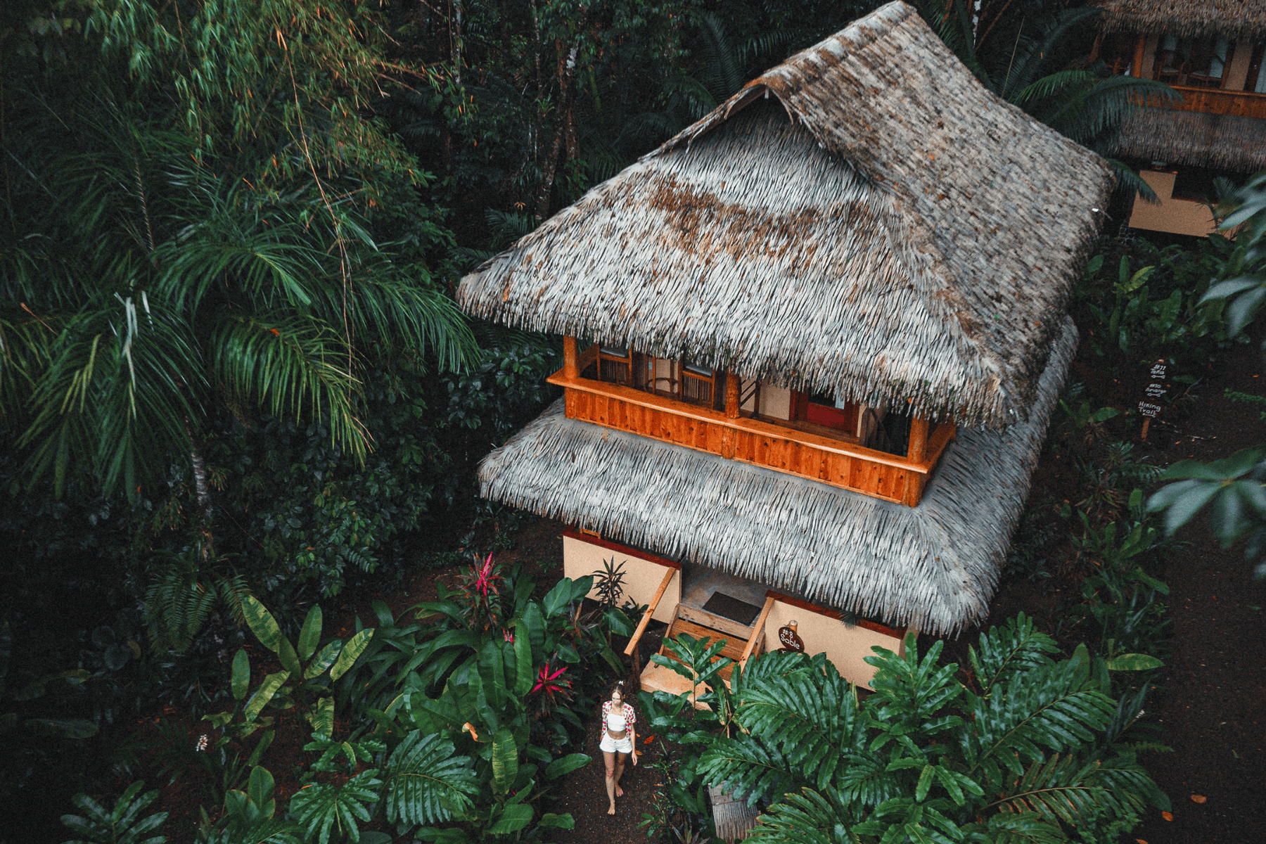 A woman standing in front of a hut surrounded by trees.