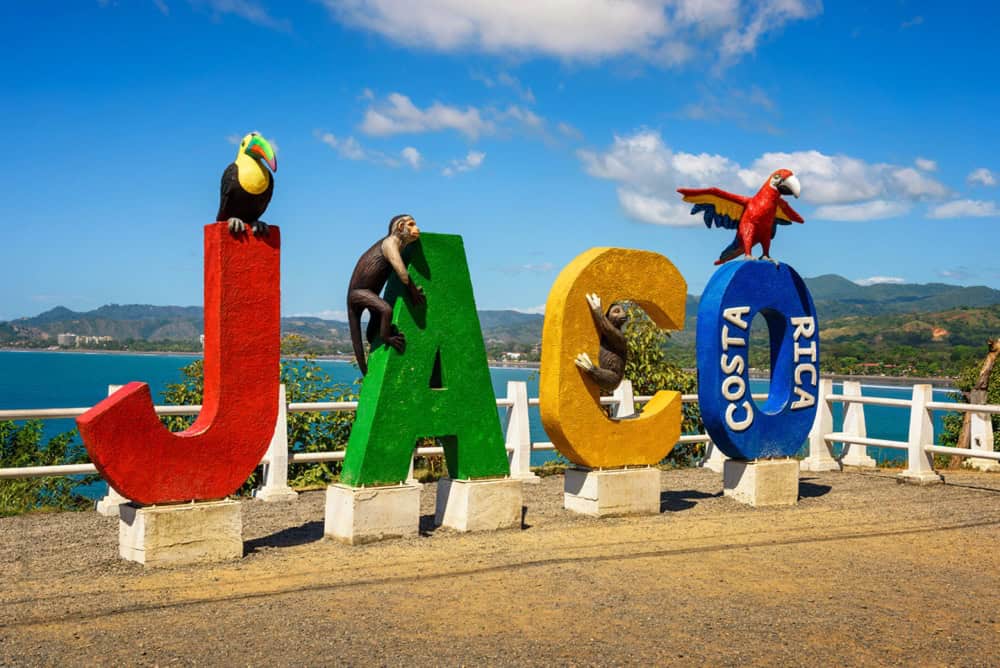 Large colorful letters spelling "JACO" with animal statues on top, set against a scenic view of the coastline and sky in Costa Rica.